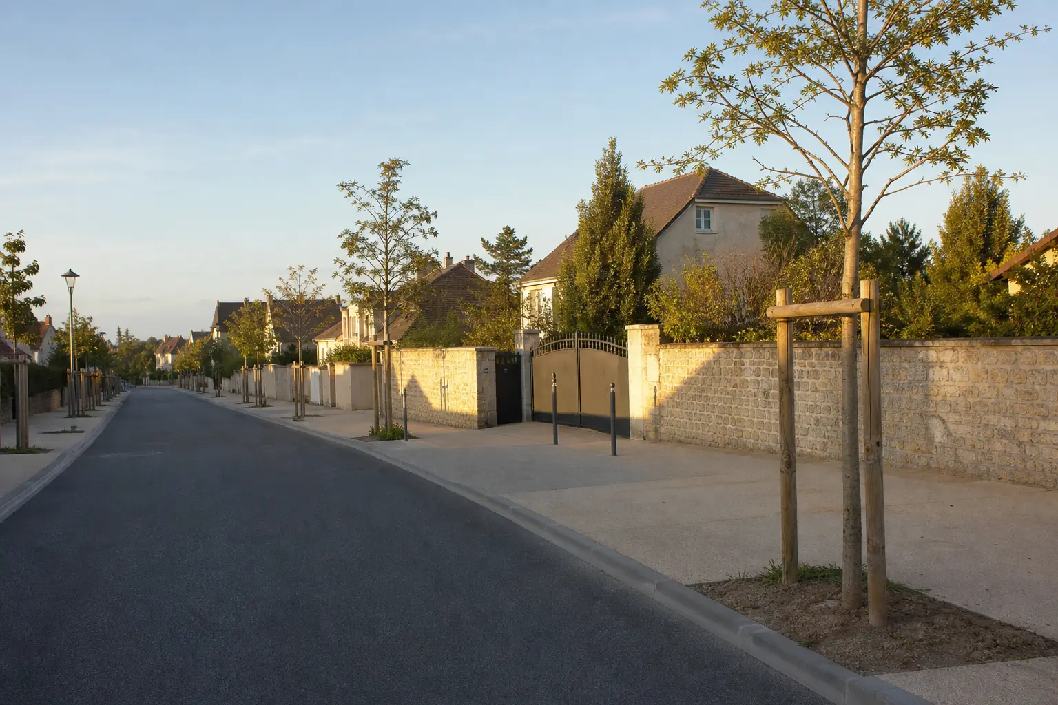 Rue résidentielle de plateau au nord de Lyon, maisons en bande et murs de clôture en pierre