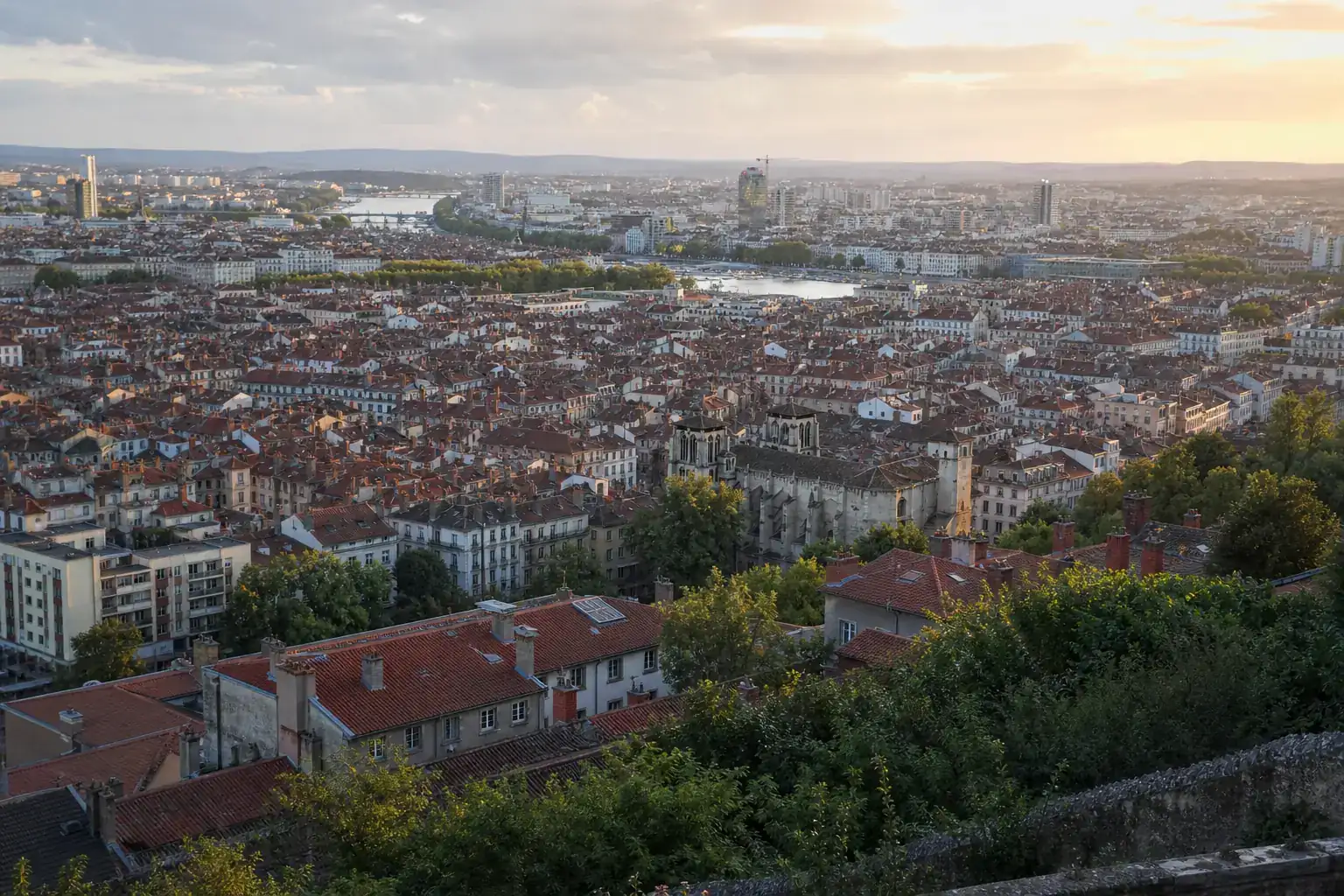 Vue large de l’agglomération lyonnaise depuis un coteau, toits de tuiles et collines à l’horizon